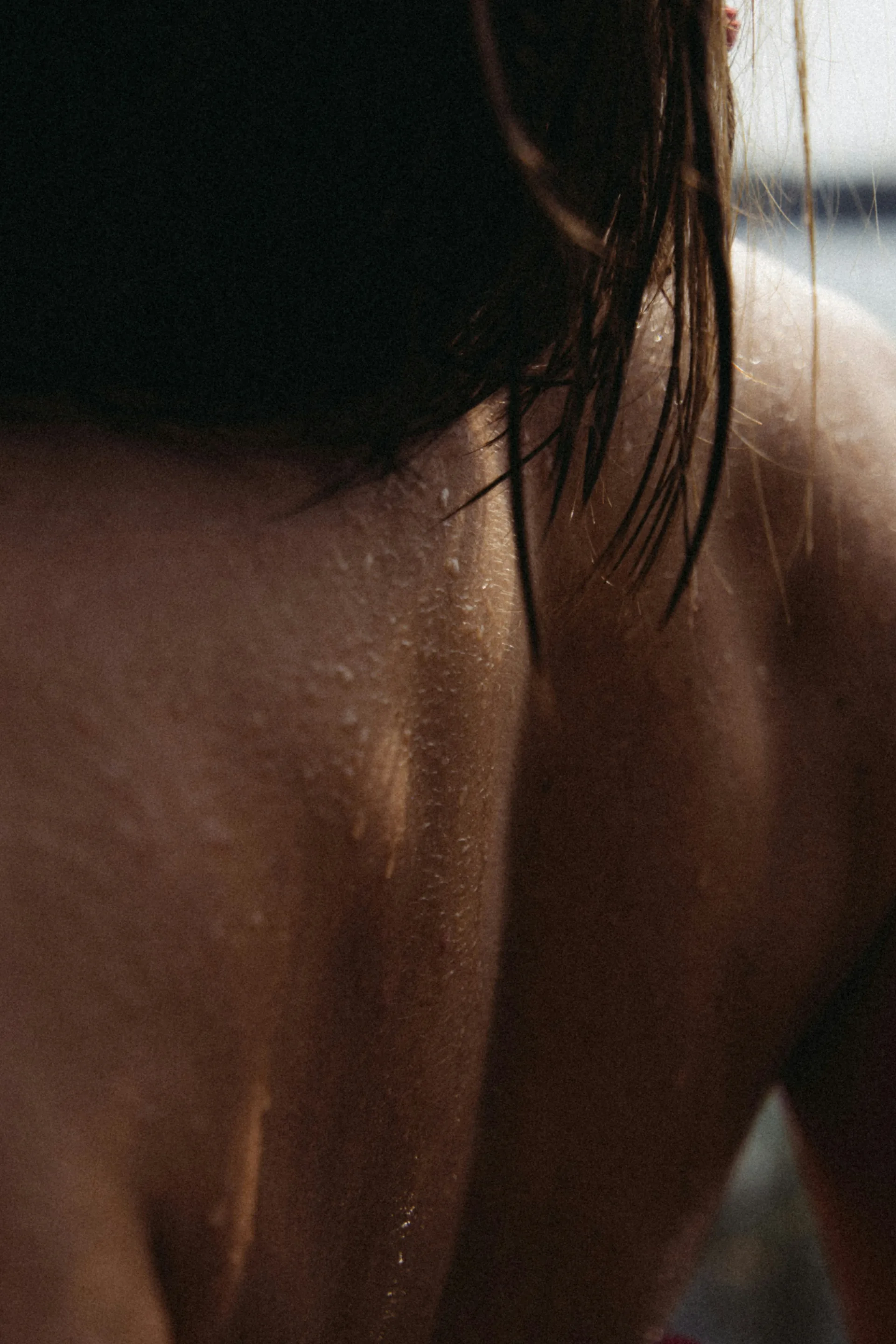 A woman's back and shoulder in warm light, skin read close.