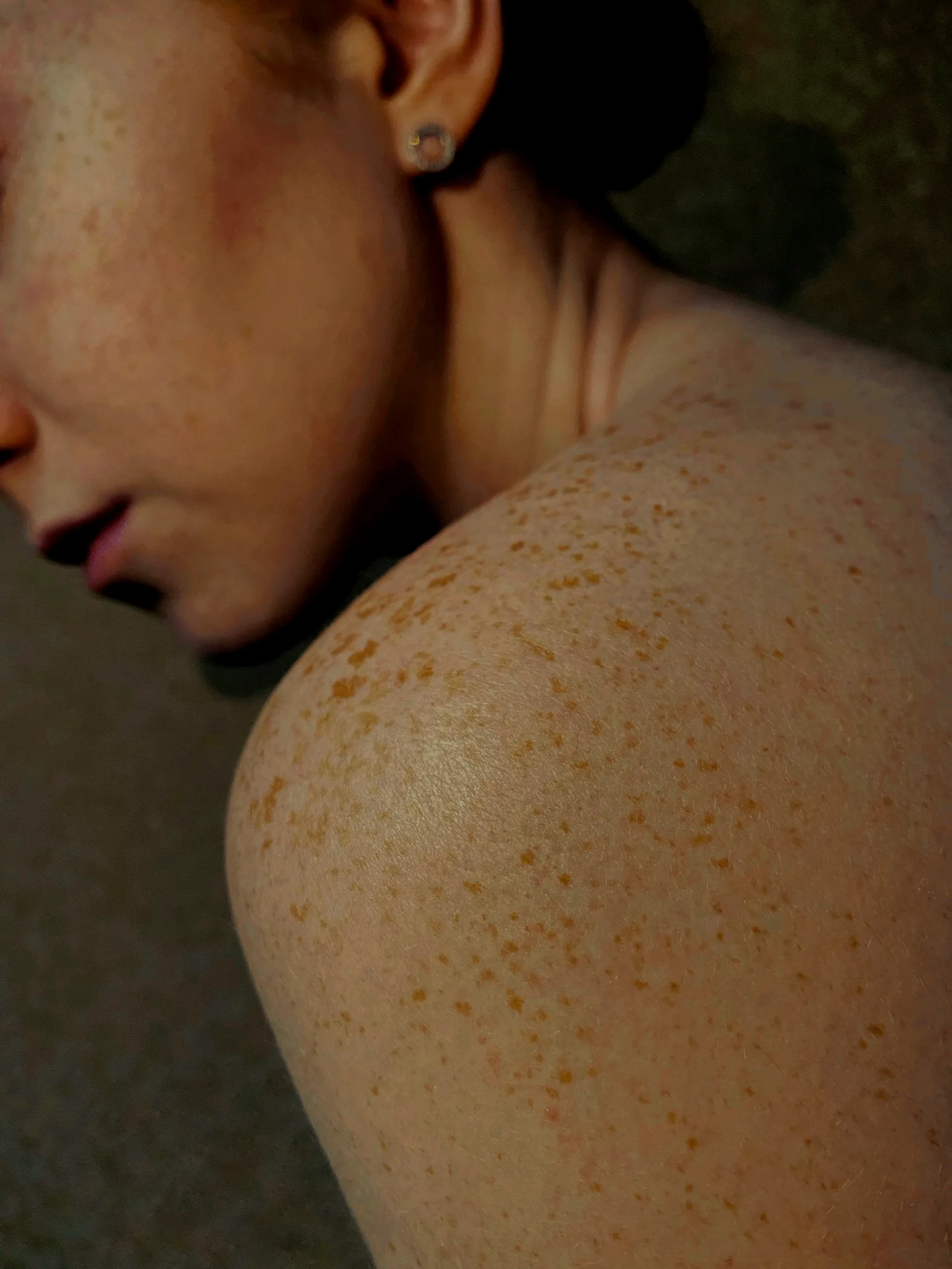 A woman turned away, freckles scattered across her shoulder read close, like a constellation.