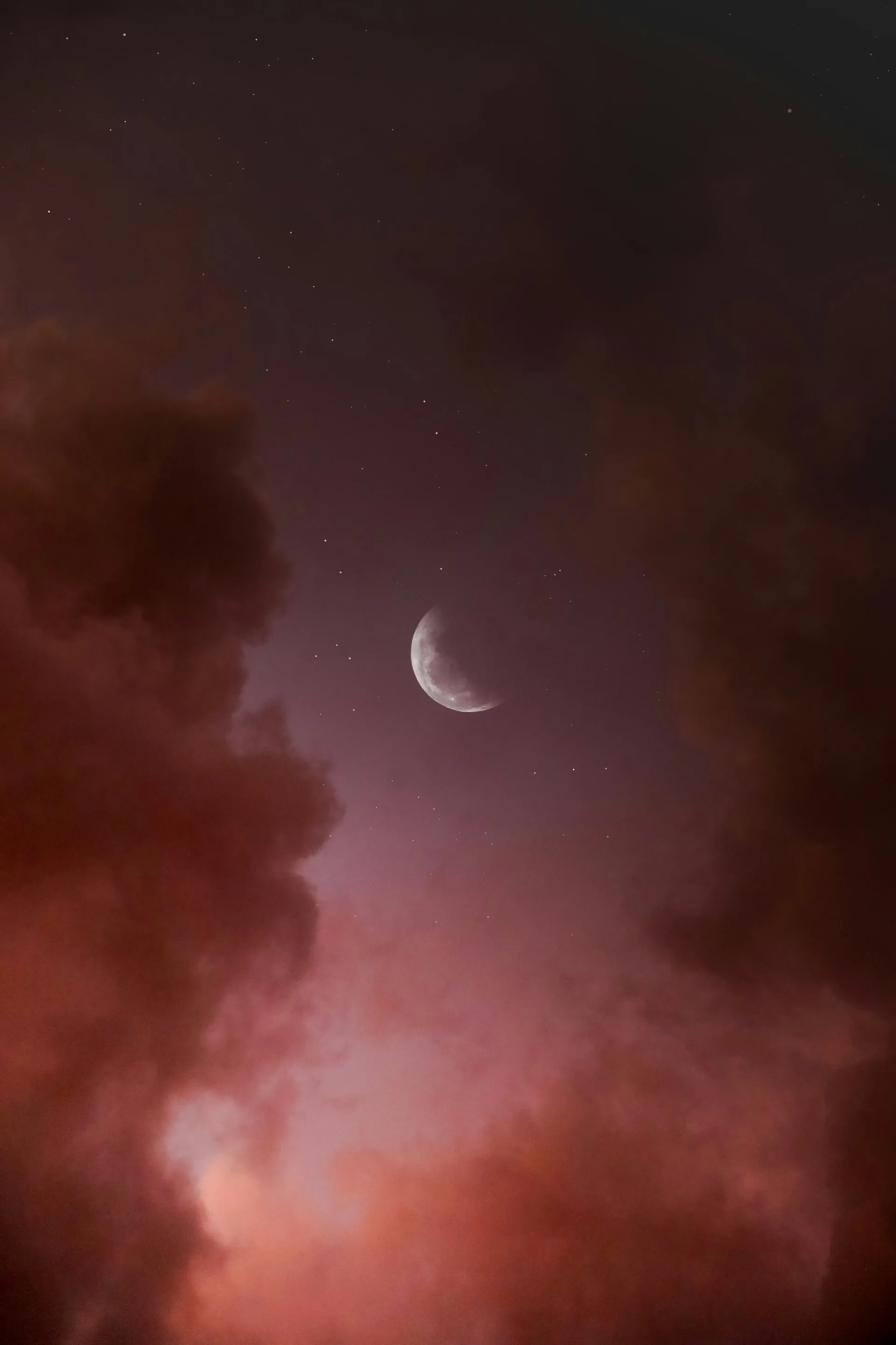 A crescent moon among faint stars, banked by rust-coloured cloud.