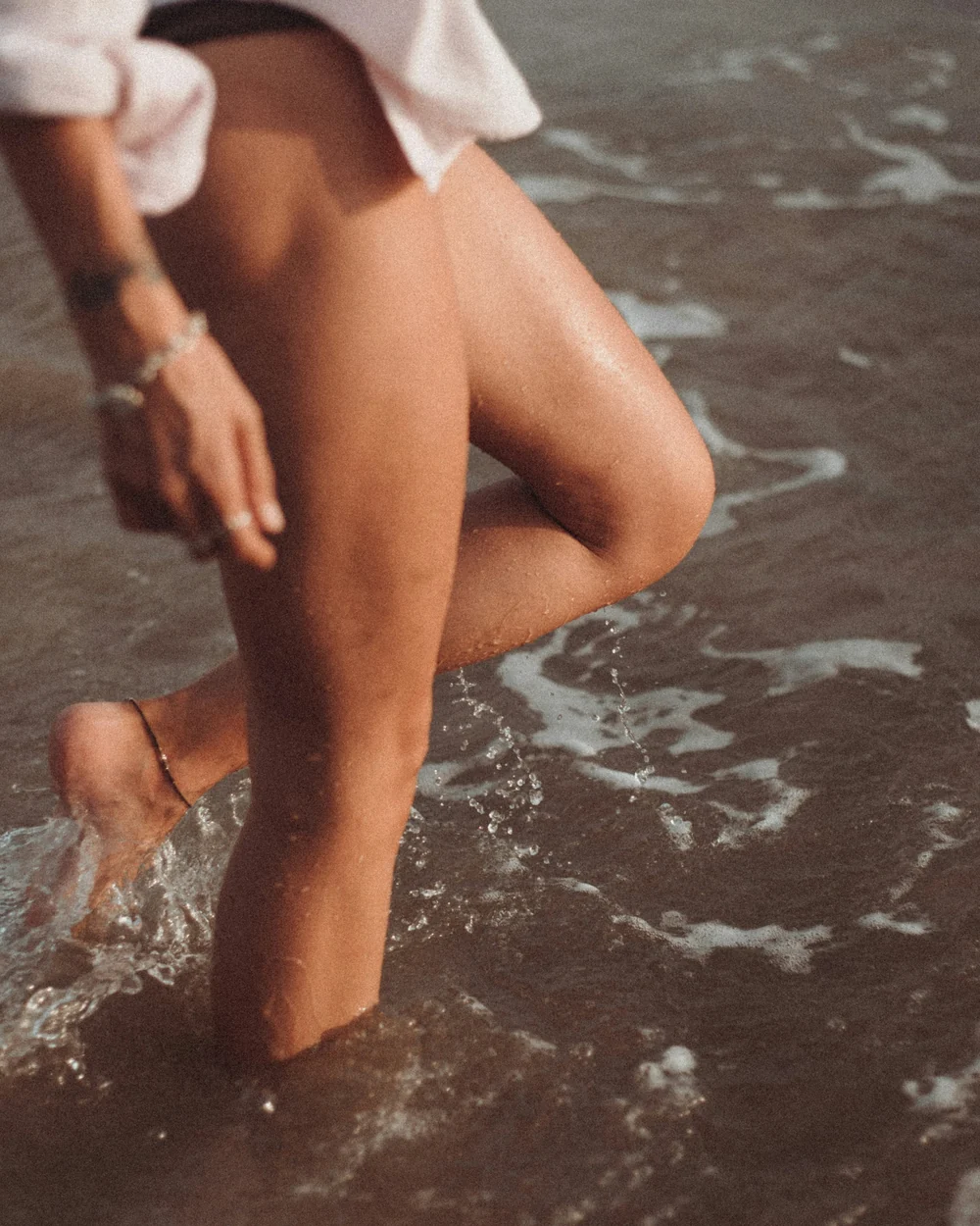 A woman walking through the shallows at the water's edge.