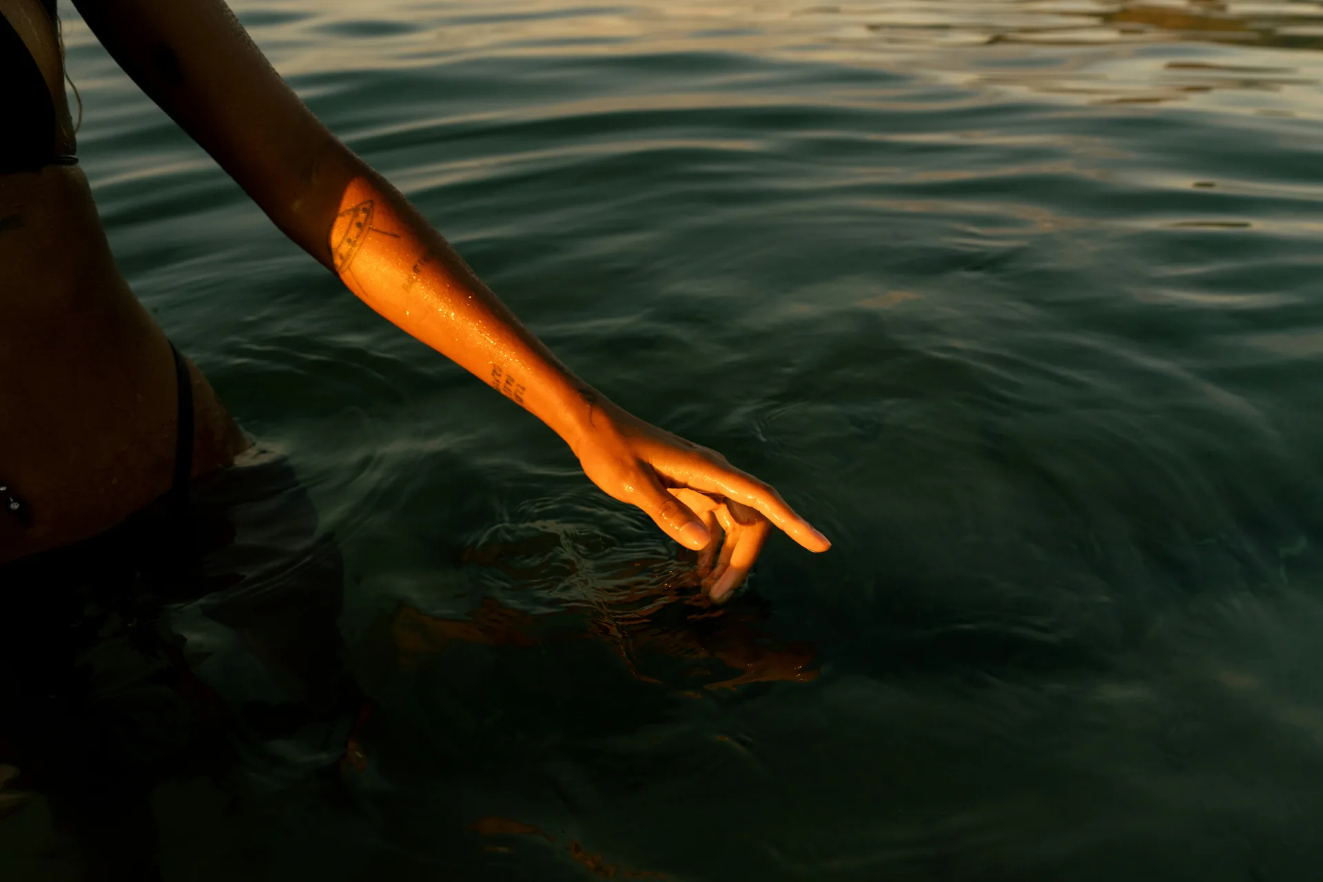 An arm reaching down to meet the surface of cool water.