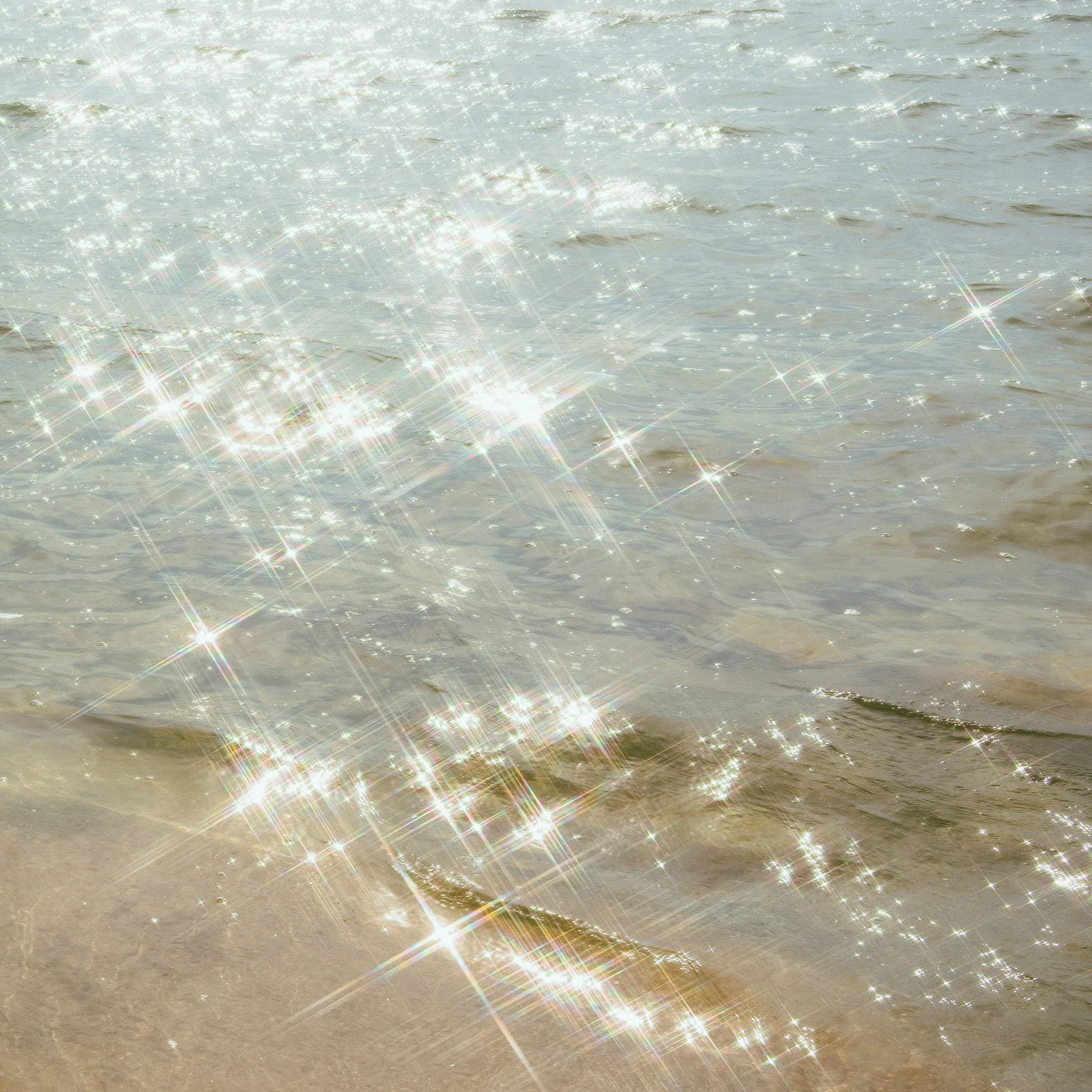 Sunlight breaking into points across shallow water over sand.