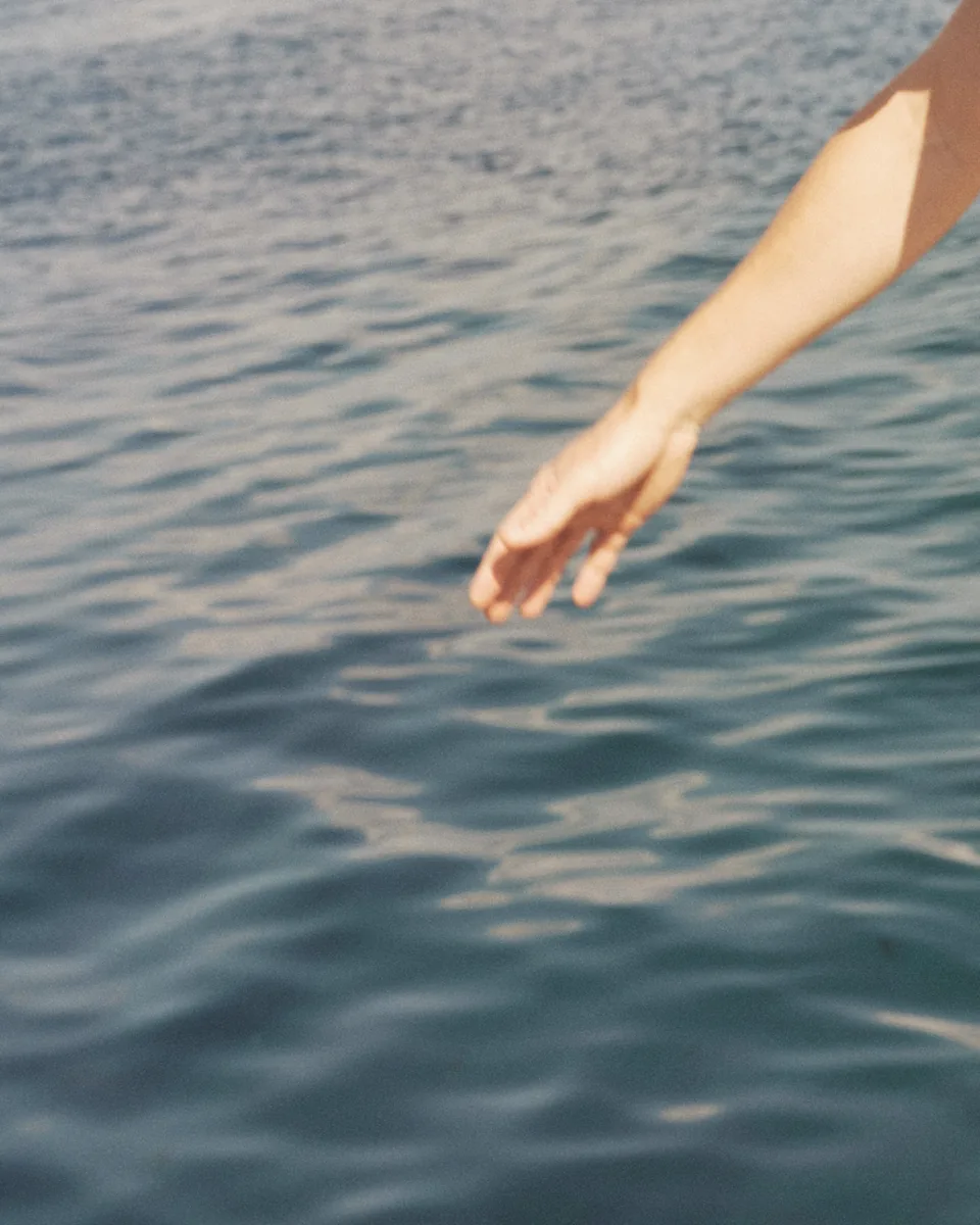 An arm reaching down to meet the surface of cool water.