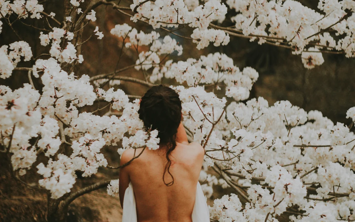 A woman standing among white blossom, turned away from the camera.