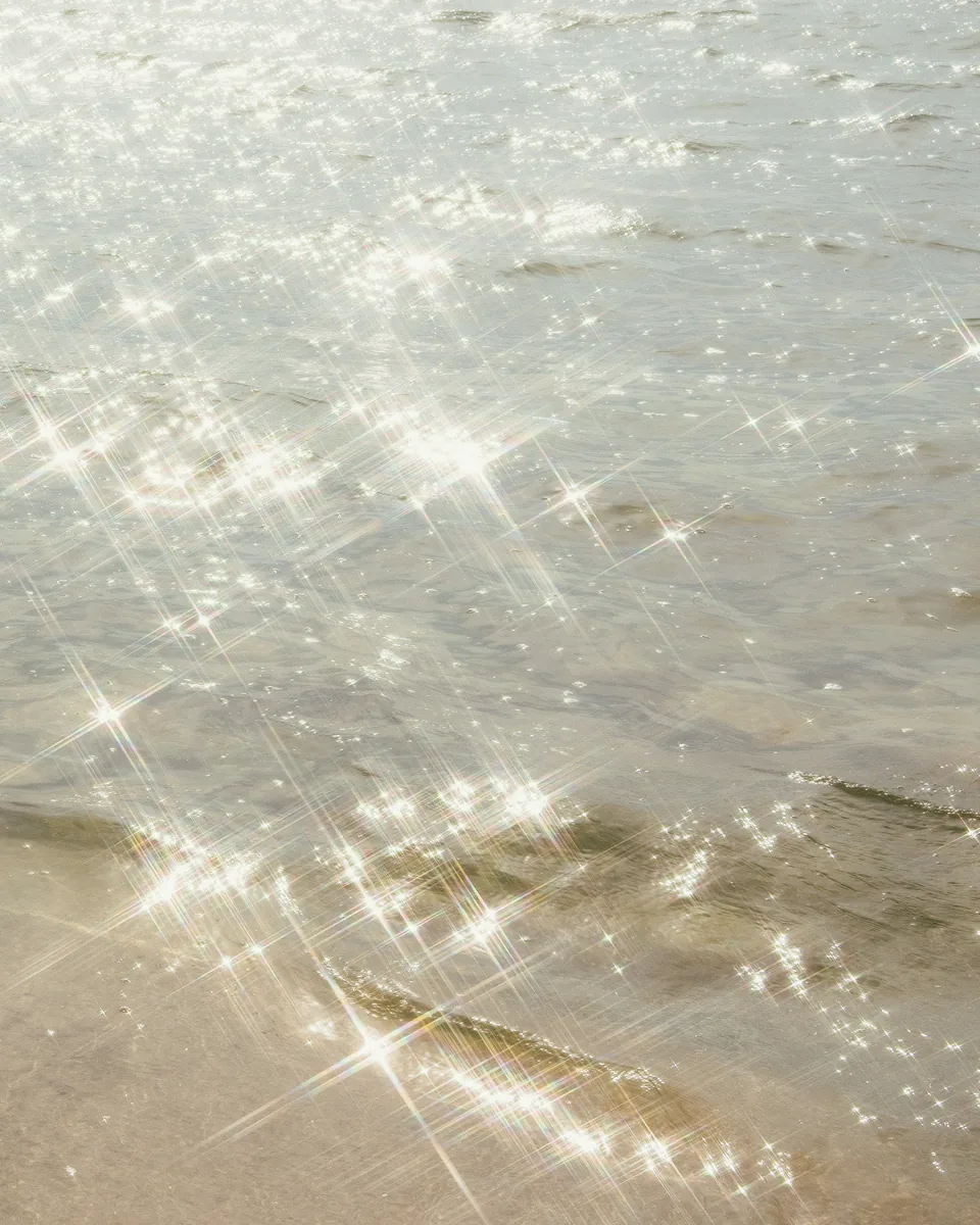 Sunlight breaking into points across shallow water over sand.