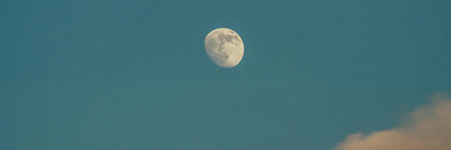 A waxing moon in a clear evening sky, cloud lit gold below.